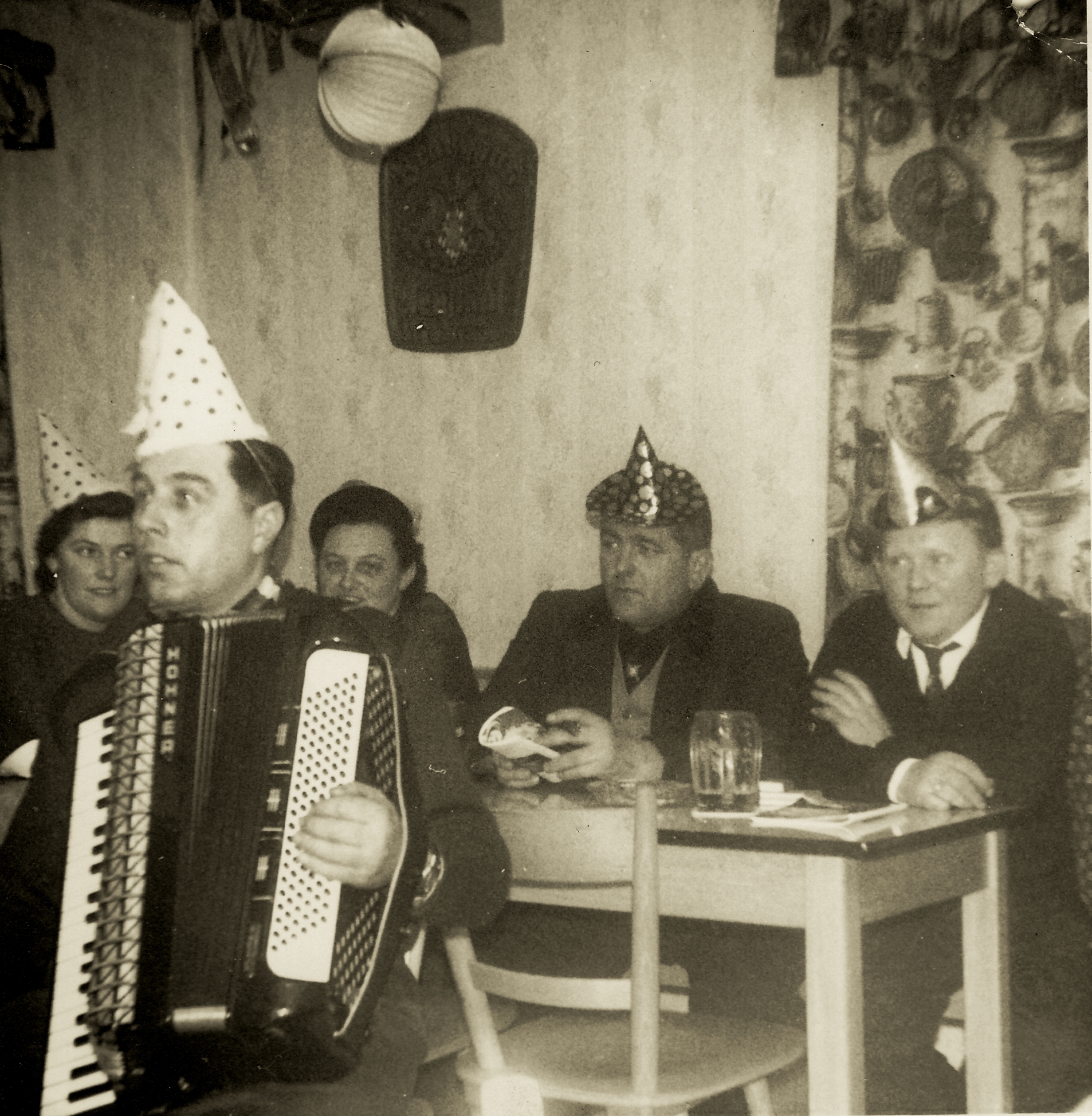 Karl Lux mit Akkordeon, vier Personen sitzen um den Tisch.
